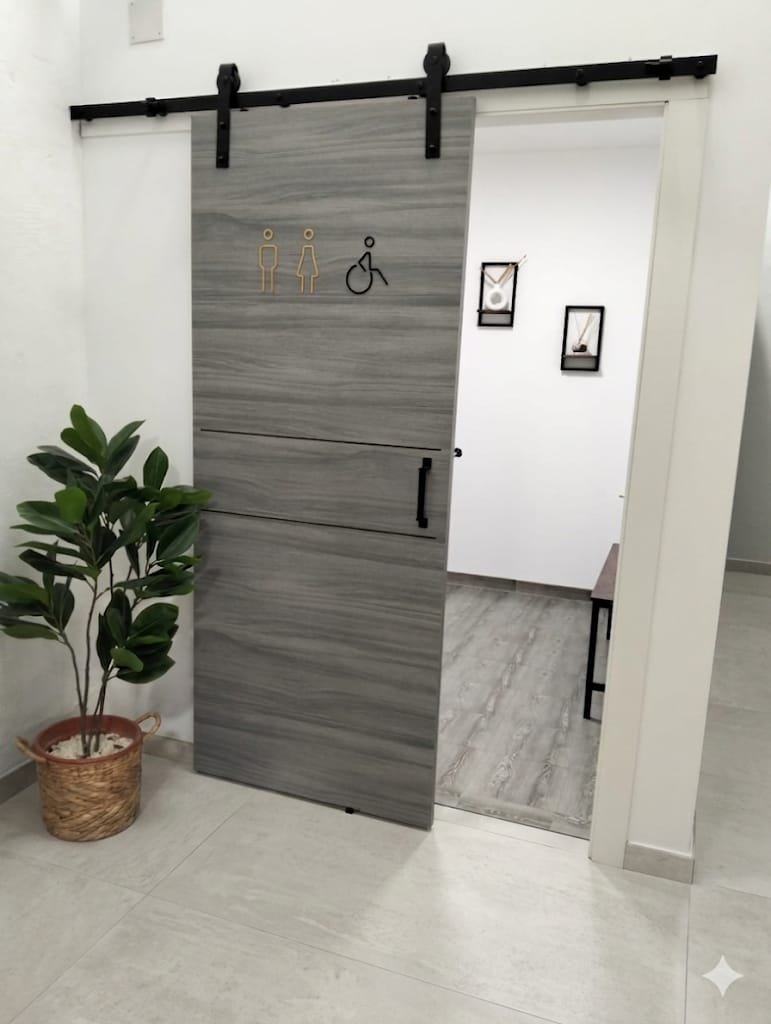 Vestíbulo y aseo accesible del estudio, con puerta corredera de madera